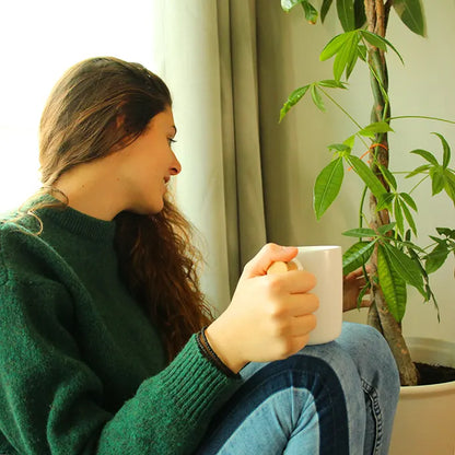 Jeune femme portant une tasse de café blanche qui regarde une plante